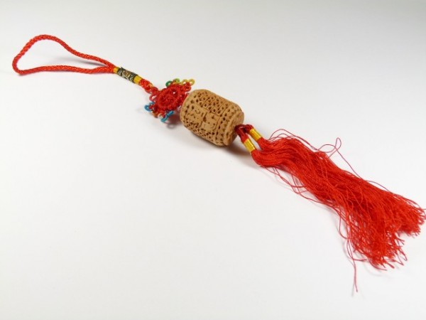 Korek od wina ozdobiony czerwonym sznurkiem i frędzlami leży na białym tle.