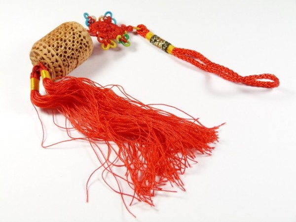 Chiński brelok z ozdobnym, czerwonym frędzlem i rzeźbionym elementem z drewna.