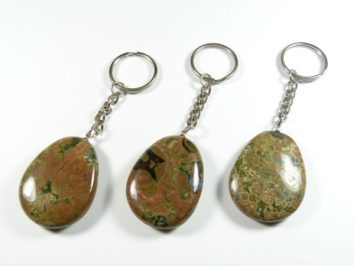 Trzy breloczki z naturalnymi, polerowanymi kamieniami na białym tle.