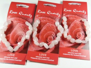 Trzy bransoletki z różowego kwarcu na czerwonych opakowaniach z napisem "Rose Quartz".