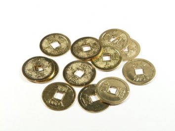 Kilka chińskich monet z kwadratowym otworem pośrodku leży na białym tle.