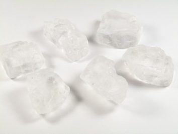 Sześć dużych, przezroczystych kryształków soli rozłożonych na białym tle.