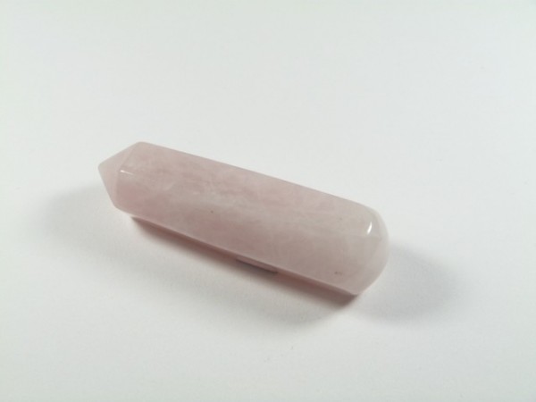 Różowy kwarc szlifowany różdżka. Różowy kryształ kwarcu o podłużnym kształcie leży na białym tle.