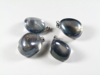 Cztery niebieskie, błyszczące zawieszki w kształcie kropli leżą na białym tle.