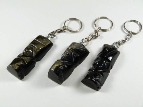 Trzy breloki z czarnymi figurkami ustawione na białym tle.