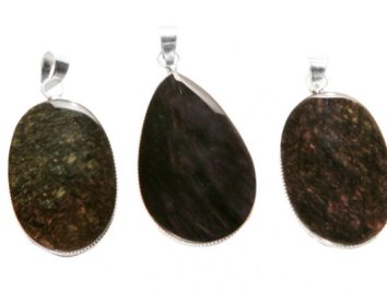 Trzy owalne wisorki z ciemnych kamieni naturalnych na białym tle.