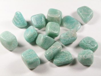 Kilka oszlifowanych, jasnozielonych kamieni leży na białym tle.