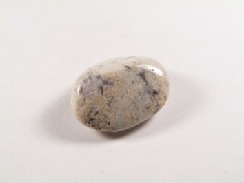 Wypolerowany, jasny kamień leży na białym tle.