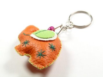 Brelok w kształcie pomarańczowego słonia z zielonymi i niebieskimi zdobieniami.