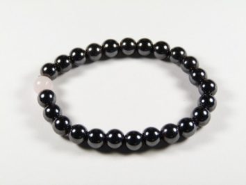 Bransoletka z czarnych koralików z jednym różowym koralikiem, na białym tle.