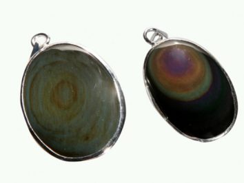 Dwa owalne wisiorki z kamieniami obsydianu w metalowych oprawach na jasnym tle.