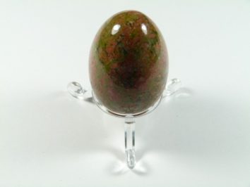 Jajko unakit szlifowany. Jajko z polerowanego kamienia na przezroczystej podstawce, sfotografowane na białym tle.