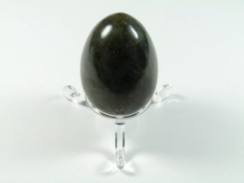 Jajko labradoryt szlifowany. Czarne jajko z kamienia na przezroczystej podstawce, na białym tle.