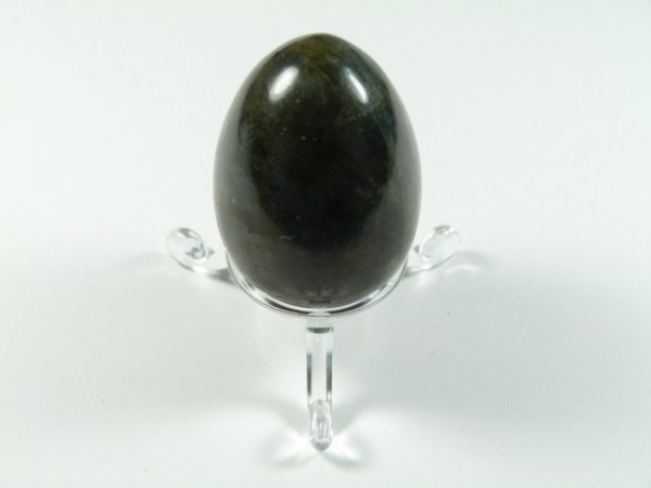 Jajko labradoryt szlifowany. Czarne jajko z kamienia na przezroczystej podstawce, na białym tle.