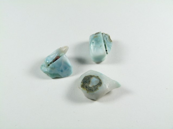 Trzy nieoszlifowane kamienie larimaru na białym tle.