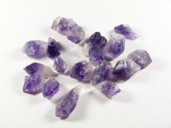 Surowe kryształy ametystu o fioletowej barwie leżące na białym tle.