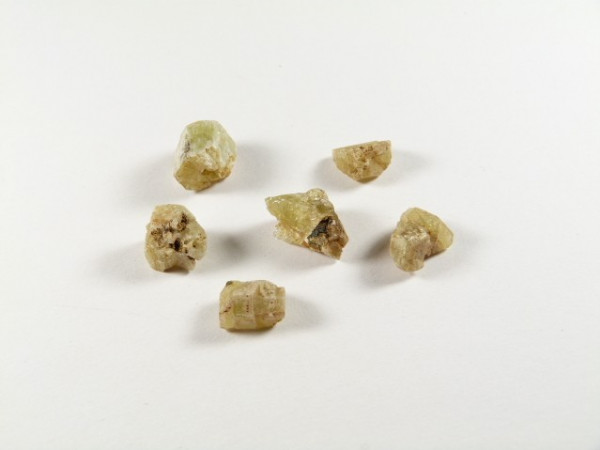 Sześć żółtawych kryształów berylu leży na białym tle.