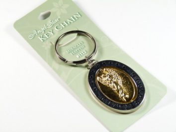 Breloczek z aniołem w złotym kolorze, przymocowany do tekturowego opakowania.