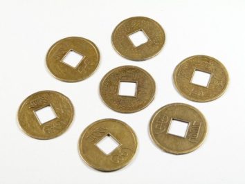 Siedem okrągłych monet z kwadratowym otworem pośrodku leży na białym tle.