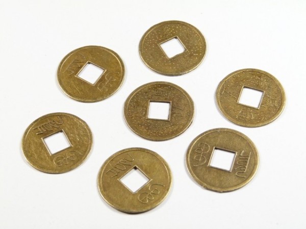 Siedem okrągłych monet z kwadratowym otworem pośrodku leży na białym tle.