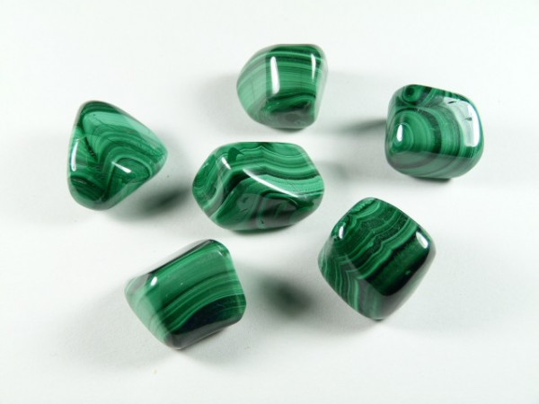 Malachit - kamień gładzony, polerowany, szlifowany i bębnowany w formie otoczaka. Sześć zielonych, wypolerowanych kamieni malachitu leży na białym tle.