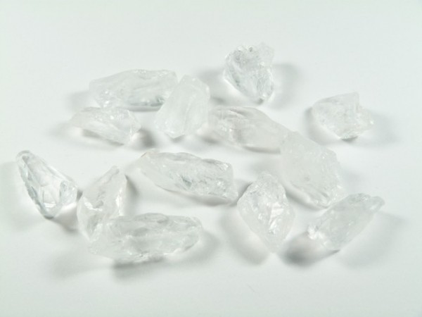 Kilka przezroczystych kryształków leży na białej powierzchni.
