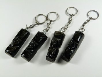 Cztery breloczki z czarnymi figurkami o rzeźbionych twarzach, ułożone na białym tle.