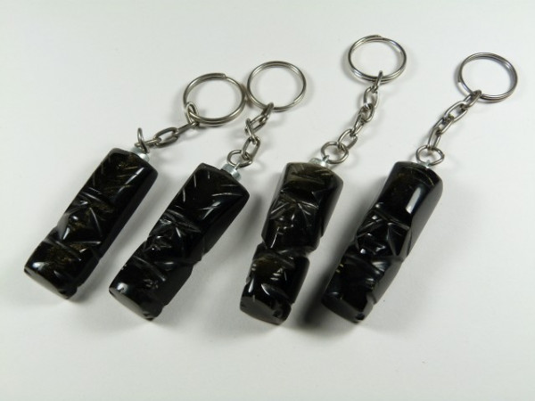 Cztery breloczki z czarnymi figurkami o rzeźbionych twarzach, ułożone na białym tle.