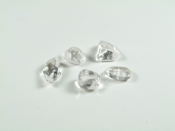 Pięć surowych, przezroczystych diamentów na białym tle.