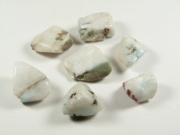 Siedem mlecznobiałych, oszlifowanych kamieni ułożonych na białym tle.