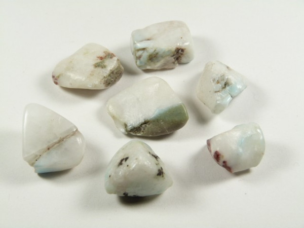 Siedem mlecznobiałych, oszlifowanych kamieni ułożonych na białym tle.