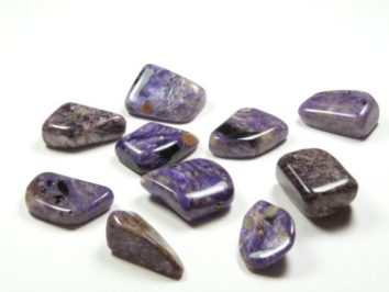 Czaroit - kamień gładzony, polerowany, szlifowany i bębnowany w formie otoczaka. Dziesięć wypolerowanych, fioletowych kamieni leży na białym tle.