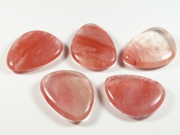 Kwarc wiśniowy szlifowany - płaski kamień. Pięć polerowanych różowych kamieni leży na białym tle.