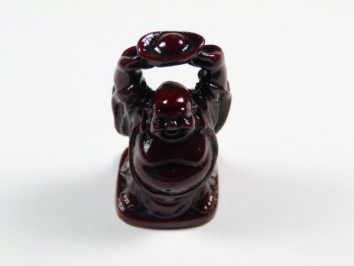 Mała figurka Buddy trzymającego nad głową okrągły przedmiot, na białym tle.