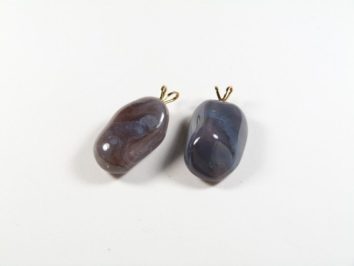 Dwa polerowane kamienie z zawieszkami leżące na białym tle.