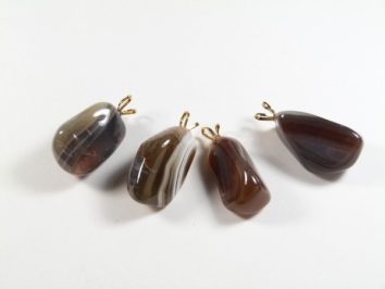 Cztery brązowe kamienie z zawieszkami, ułożone na białym tle.