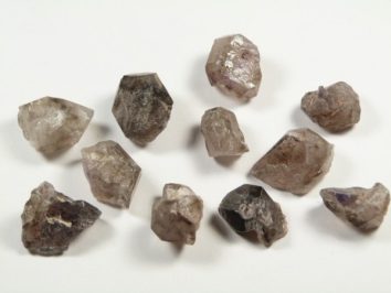 Lepidokrocyt - kamień naturalny, surowy, nieszlifowany. Jedenaście surowych kryształów leży na białym tle, nieregularne kształty.