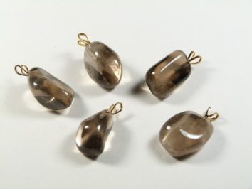 Pięć brązowych kamieni z zawieszkami leży na białym tle.