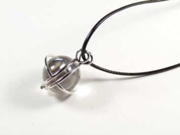 Srebrny wisior z kulistym wisiorkiem na czarnym rzemyku, na białym tle.