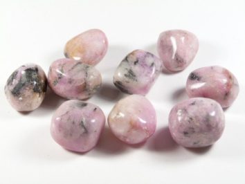 Dziewięć wypolerowanych, różowych kamieni leży na białym tle.