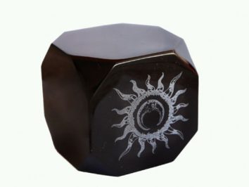 Czarny sześcian z wygrawerowanym białym symbolem słońca na jednej ze ścian.