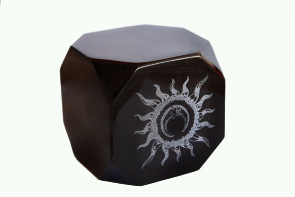 Czarny sześcian z wygrawerowanym białym symbolem słońca na jednej ze ścian.