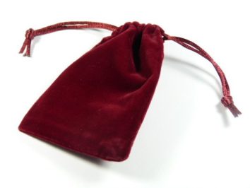 Bordowy woreczek z aksamitu ściągnięty sznurkiem, leży na białym tle.