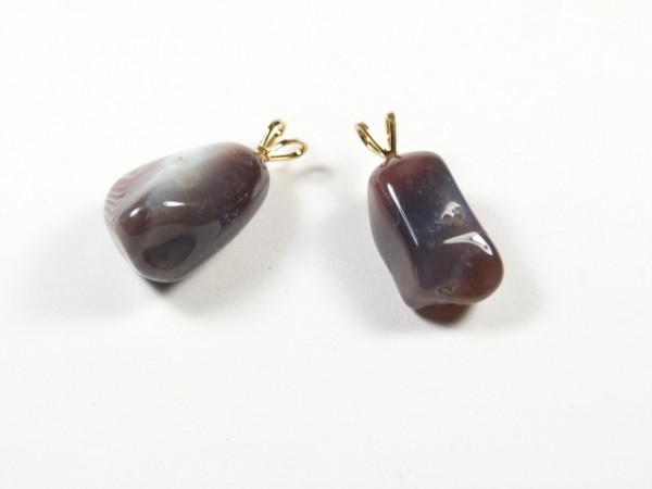 Dwa brązowo-szare kamienie z metalowymi zawieszkami leżą na białym tle.