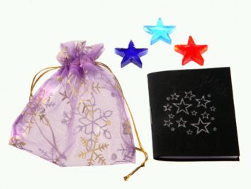 Fioletowy woreczek, czarny notes ze srebrnymi gwiazdami i trzy kolorowe gwiazdki obok.