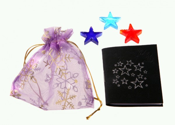 Fioletowy woreczek, czarny notes ze srebrnymi gwiazdami i trzy kolorowe gwiazdki obok.