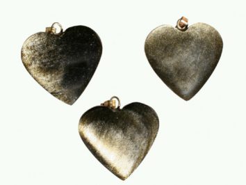 Trzy metalowe zawieszki w kształcie serca na jasnym tle.