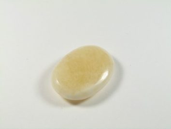 Jasnożółty, wygładzony kamień leży na białym tle.
