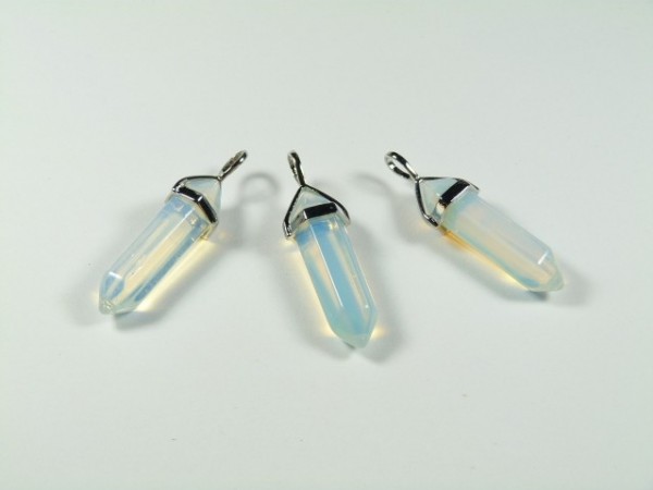 Trzy opalizujące kryształy z metalowymi zawieszkami leżące na białym tle.