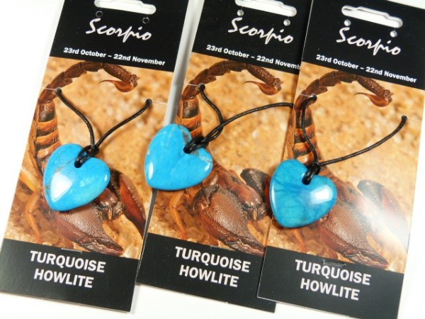 Trzy zawieszki z turkusowego howlitu w kształcie serca na tle grafiki ze skorpionem.